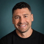 Smiling man in a black shirt against a teal studio background