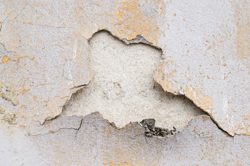 Damaged wall: cracked and peeling layers of off-white and tan paint, exposing the underlying plaster.