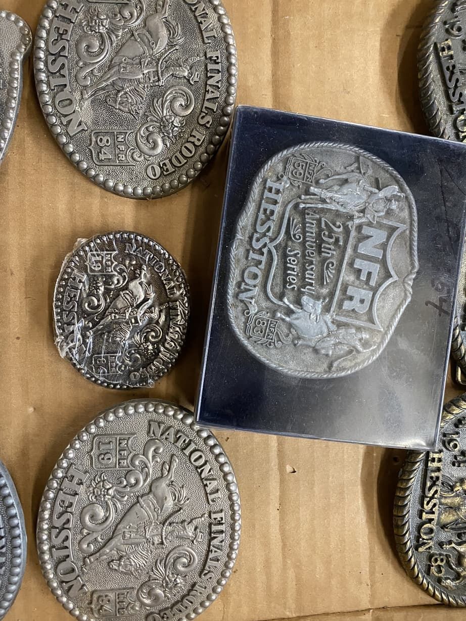A group of silver belt buckles are sitting on a cardboard box.
