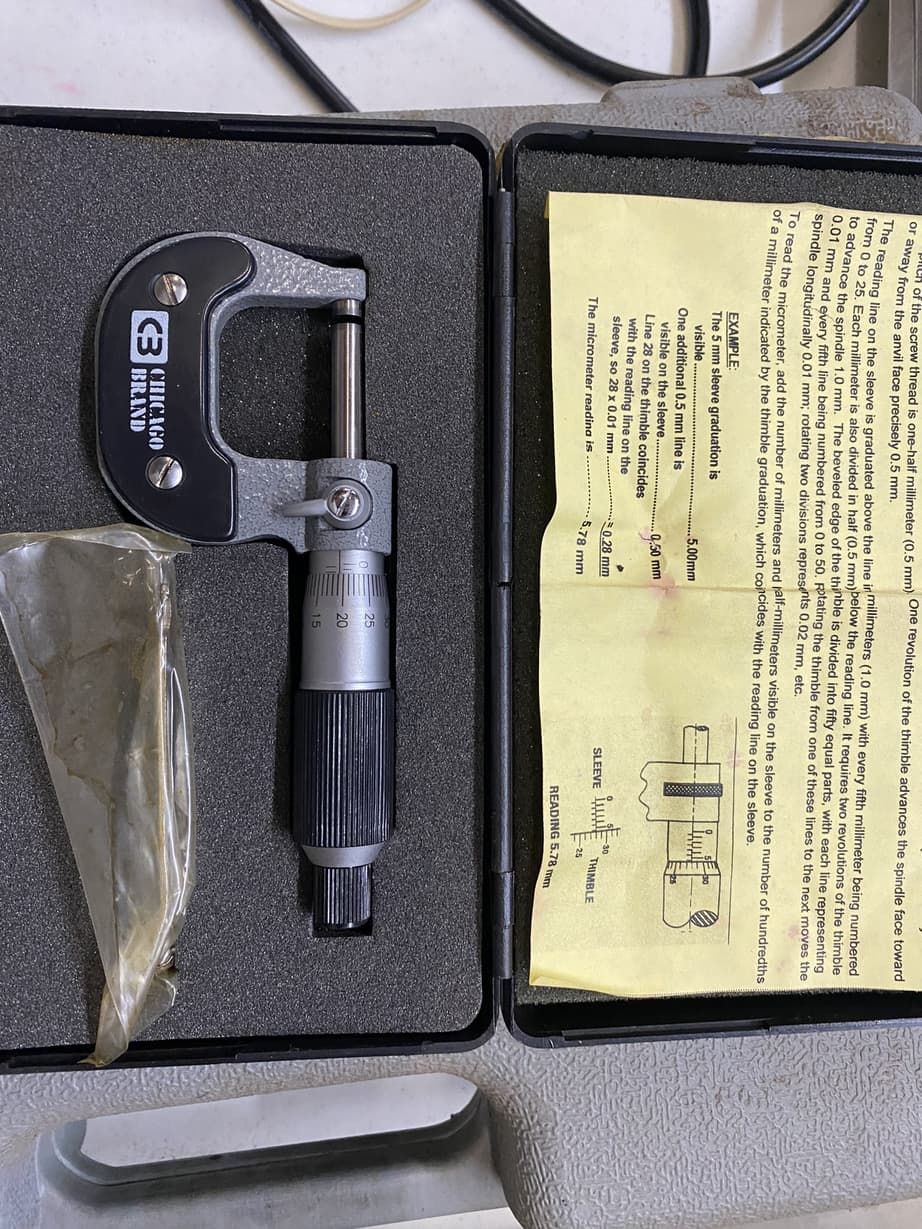A micrometer is sitting in a case next to a manual.