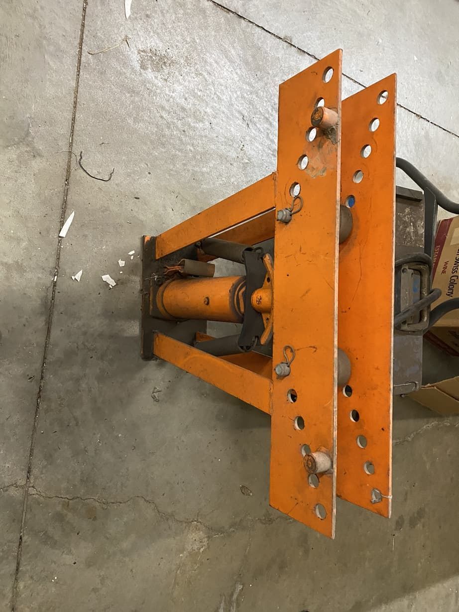 An orange pipe bending machine is sitting on a concrete floor.