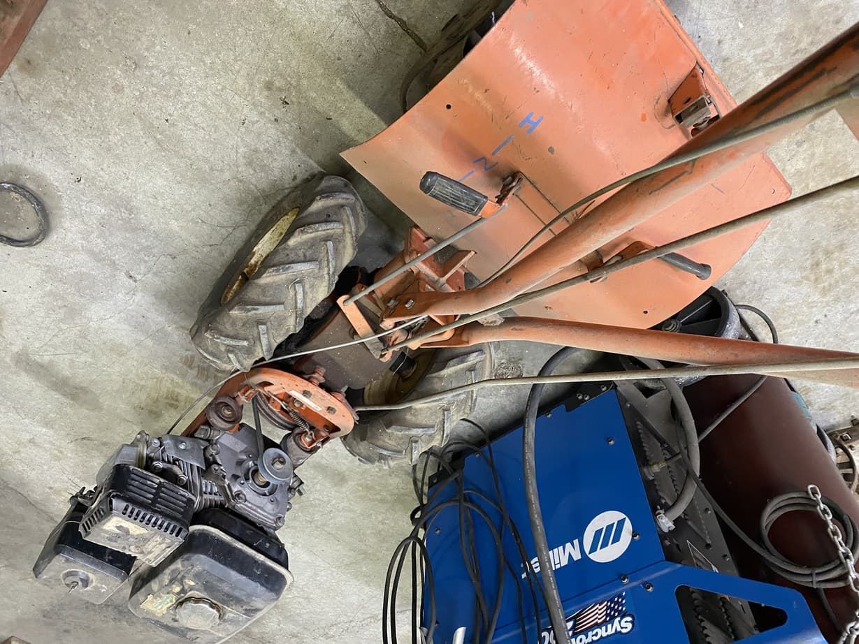 A tractor is sitting on the ground next to a welding machine.