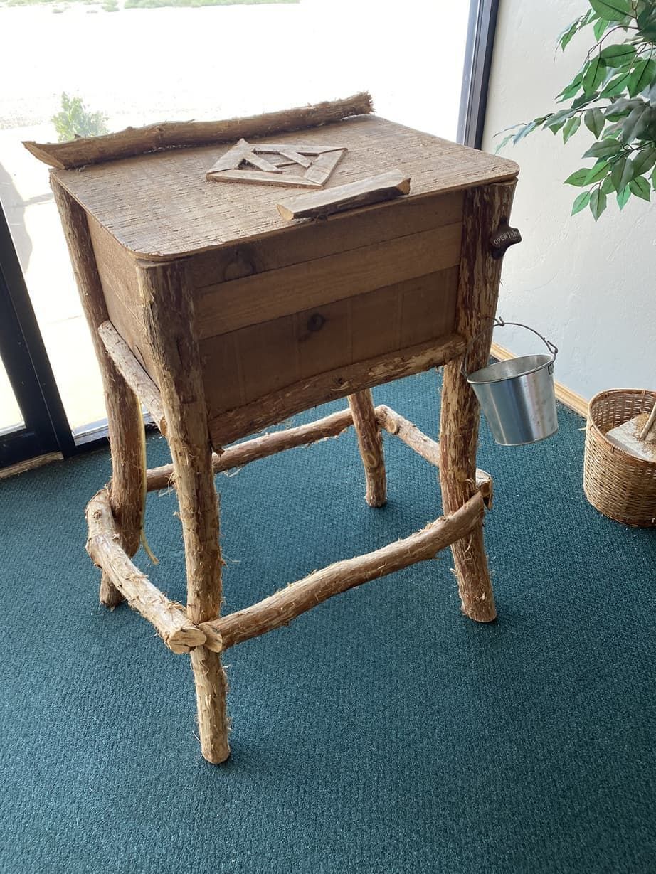 A wooden table with a drawer made out of branches is sitting on a green carpet.