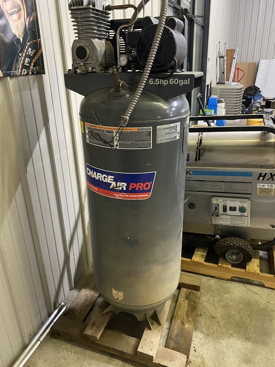 An air compressor is sitting on top of a wooden pallet in a garage.