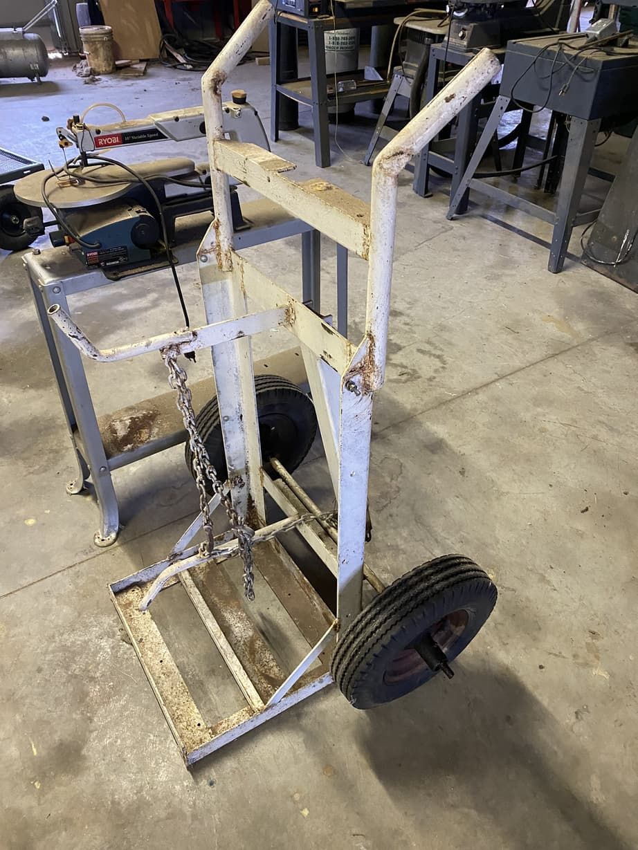 A metal cart with wheels is sitting on the floor in a garage.