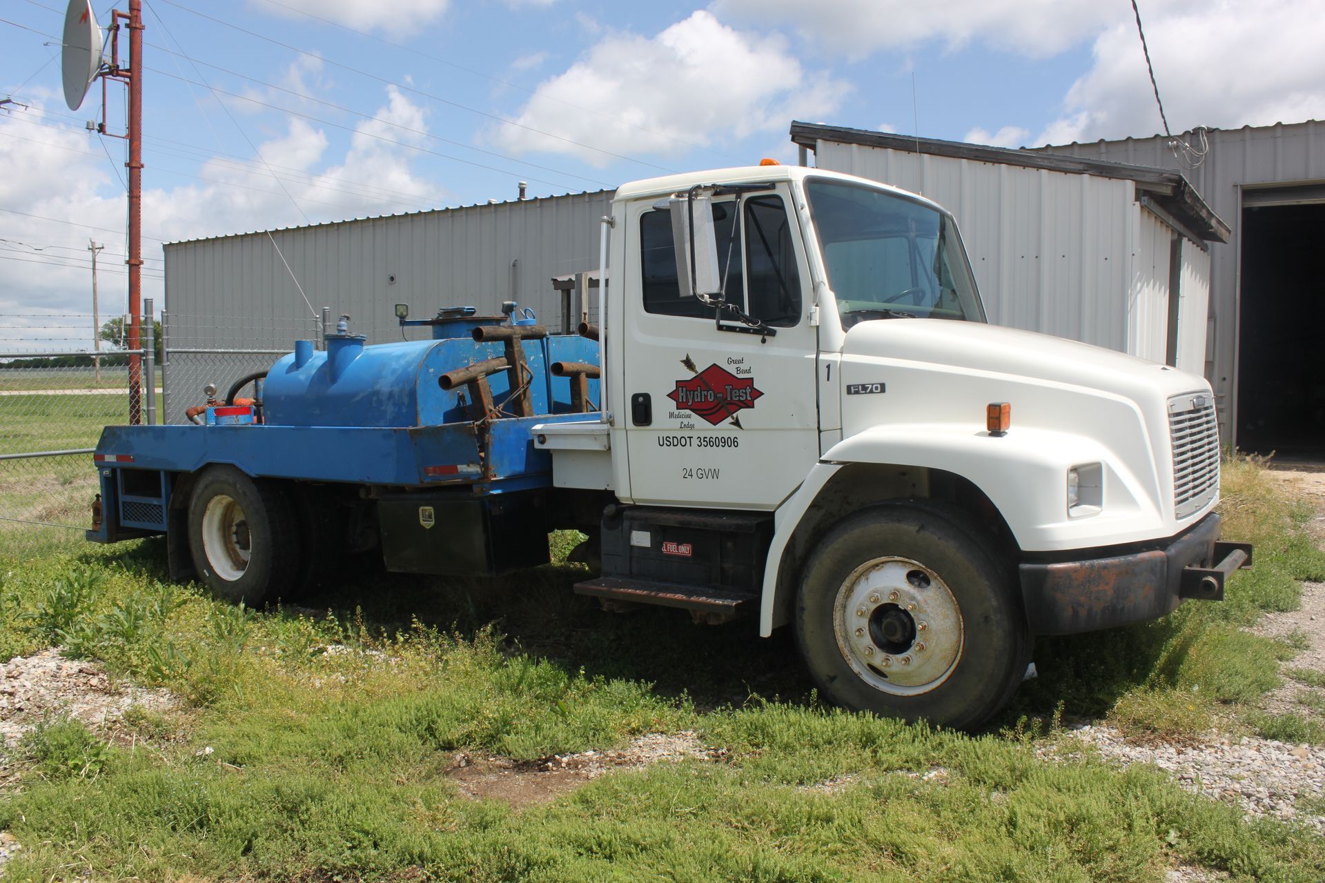 A white truck is parked in a grassy field in front of a building