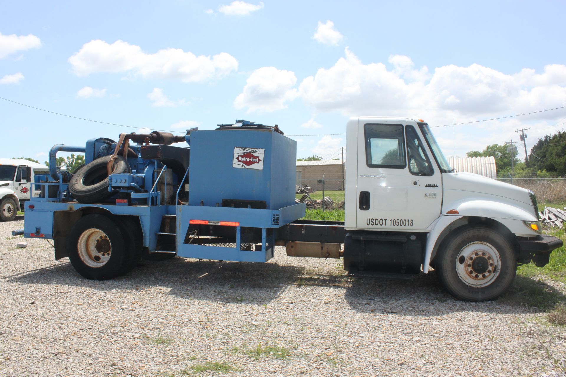 A blue and white hydro testing truck is parked in a gravel lot