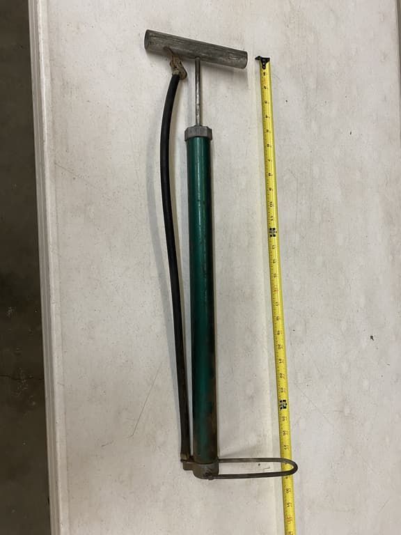 A bicycle pump is sitting next to a tape measure on a table.