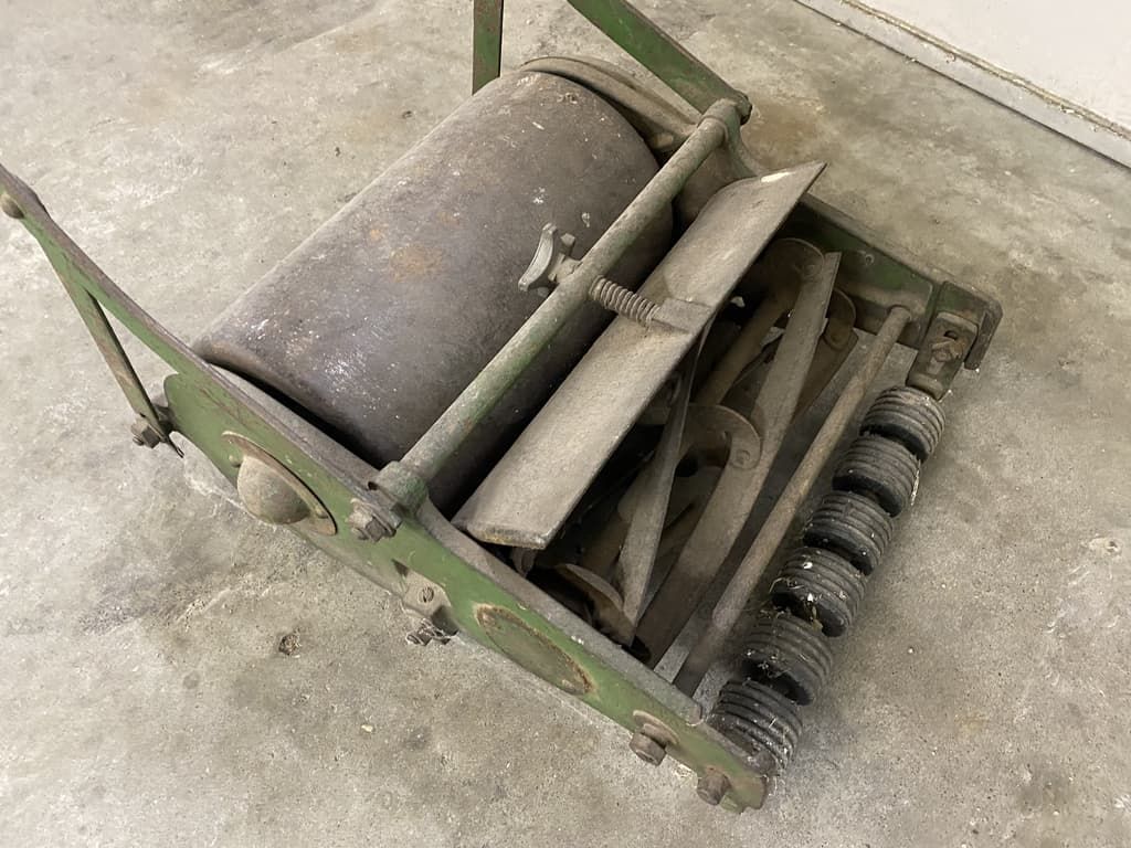 An old lawn mower is sitting on a concrete floor.