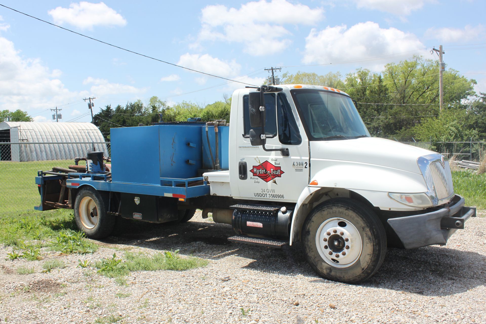 A white truck with a blue trailer is parked in a gravel lot