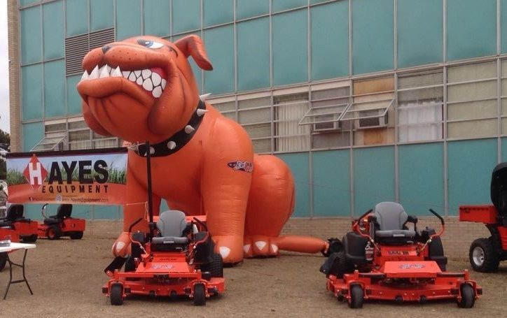 An inflatable bulldog is sitting next to a hayes lawn mower