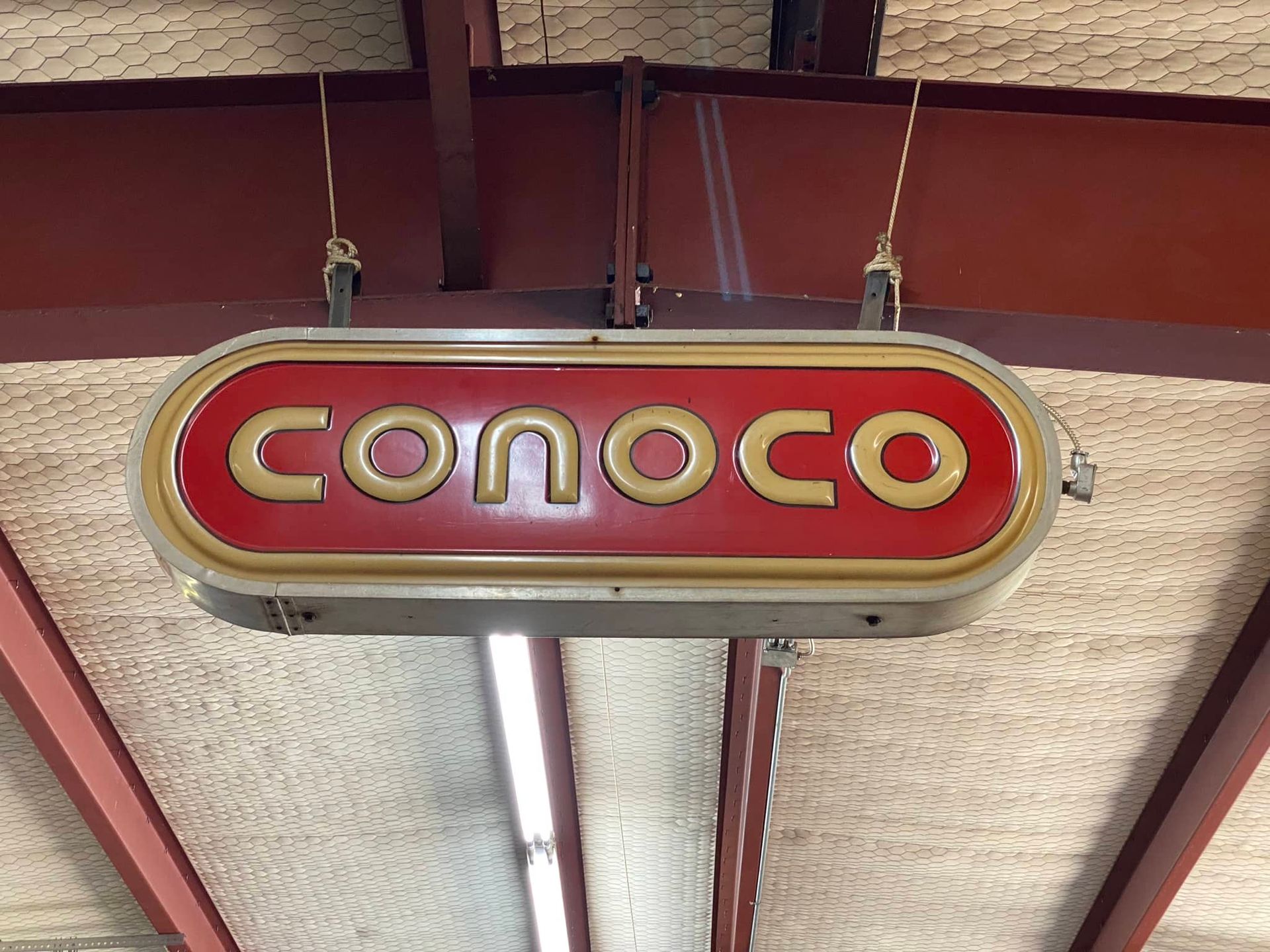 A red and gold sign that says conoco hanging from the ceiling