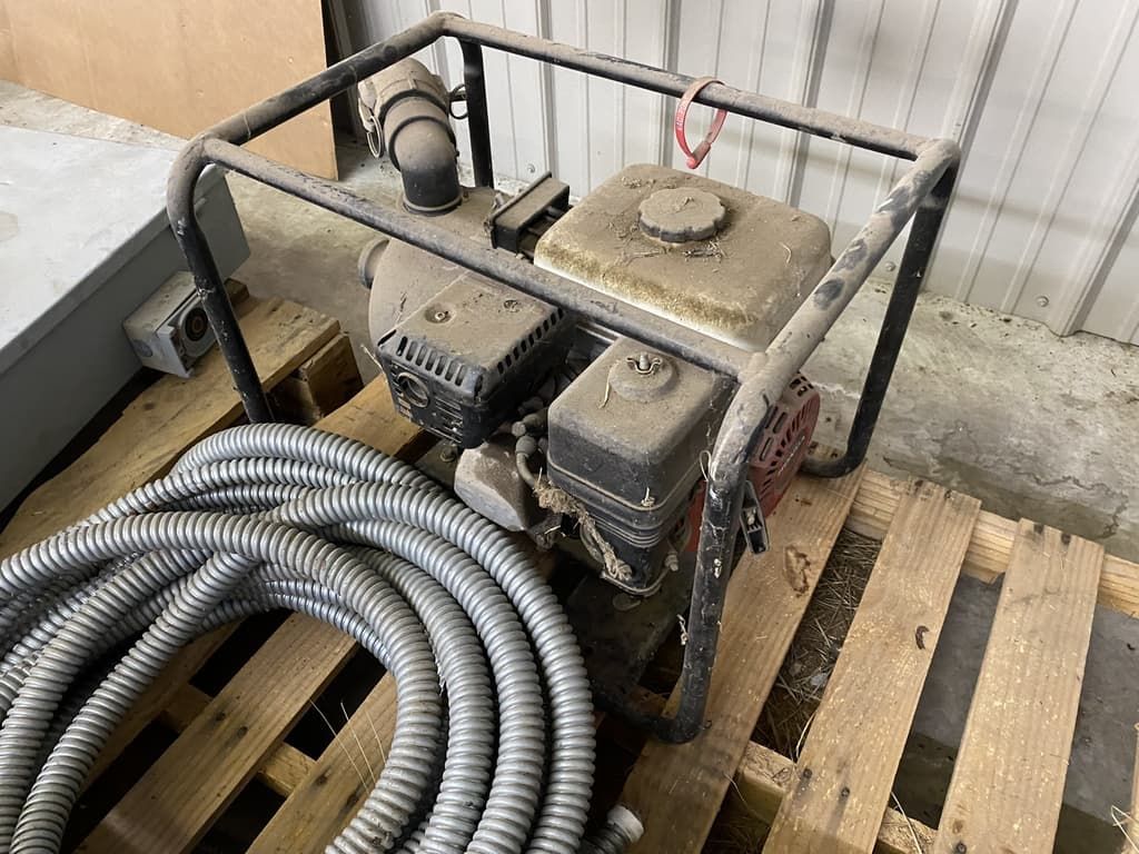 A gas engine is sitting on top of a wooden pallet next to a hose.