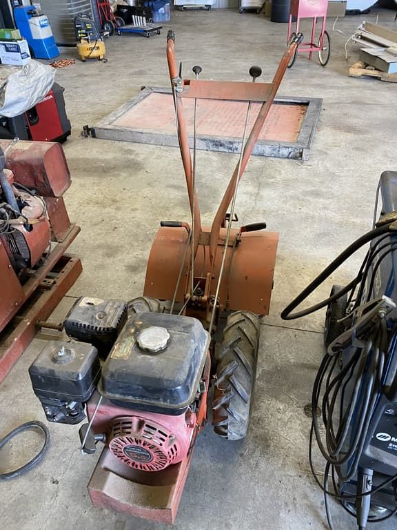 A small tractor with a gas engine is sitting in a garage.