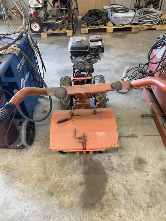 A small orange tractor is sitting on a concrete floor in a garage.