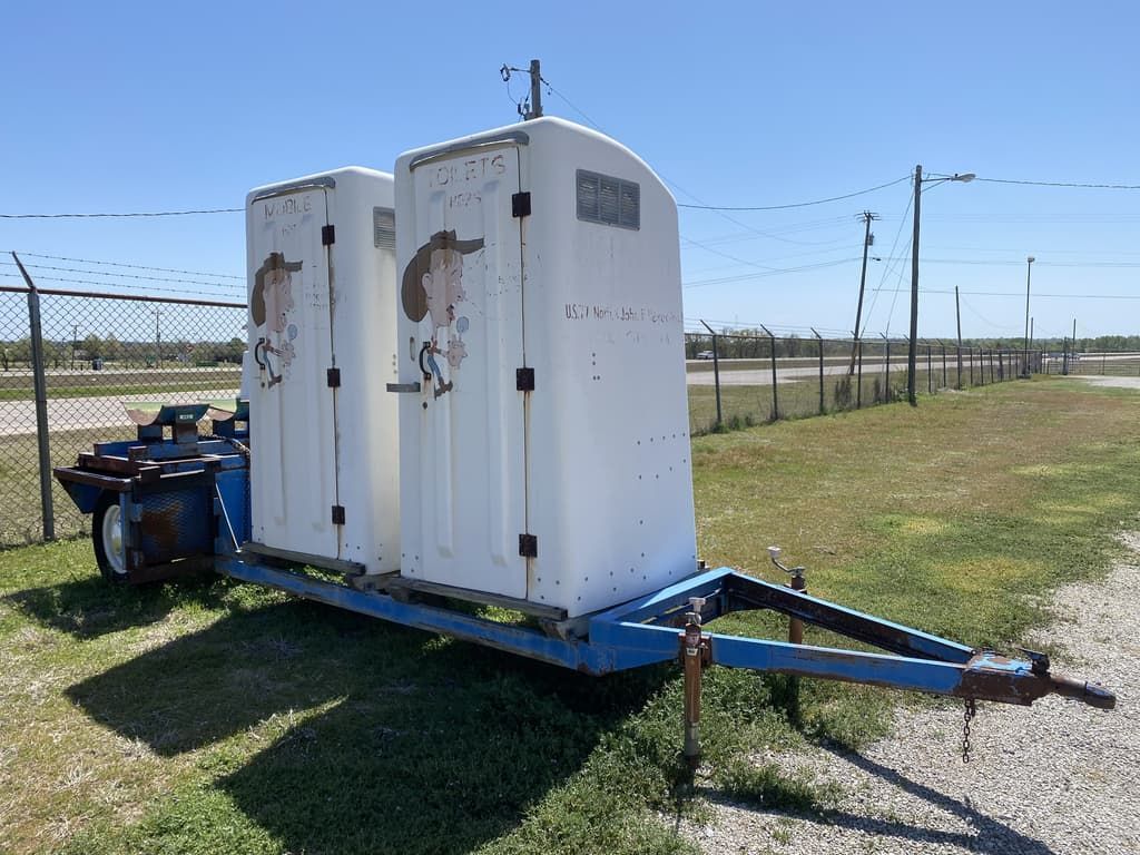 A trailer with two toilets on it is parked in a grassy field.