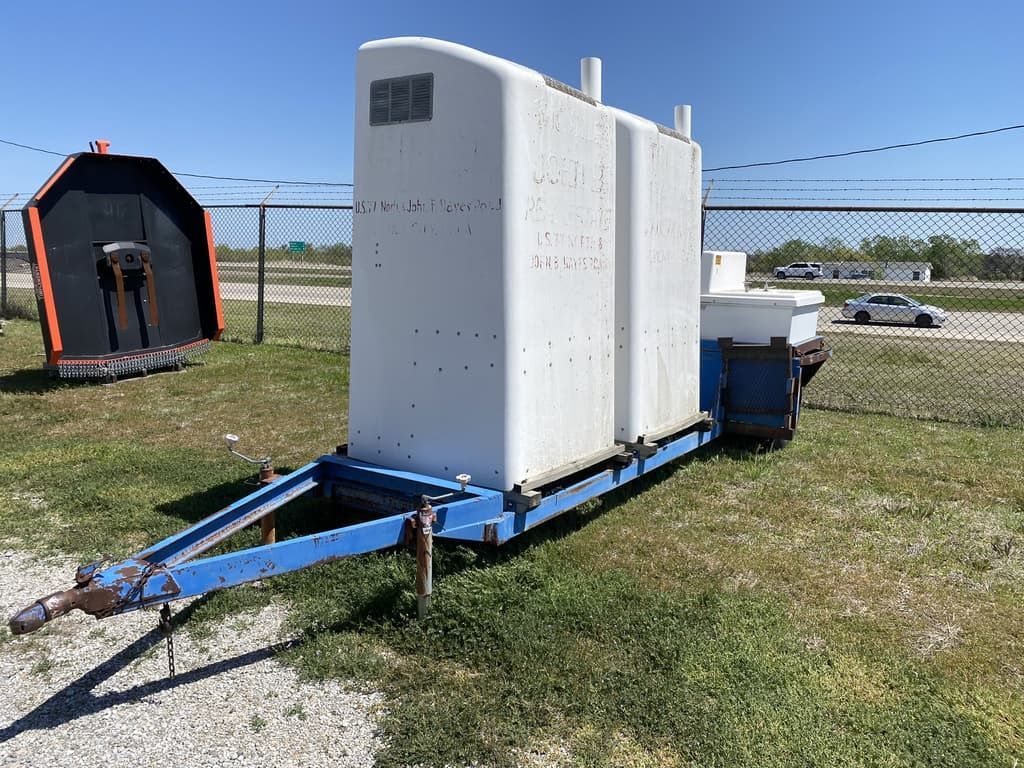 A white trailer is parked in a grassy field next to a fence.