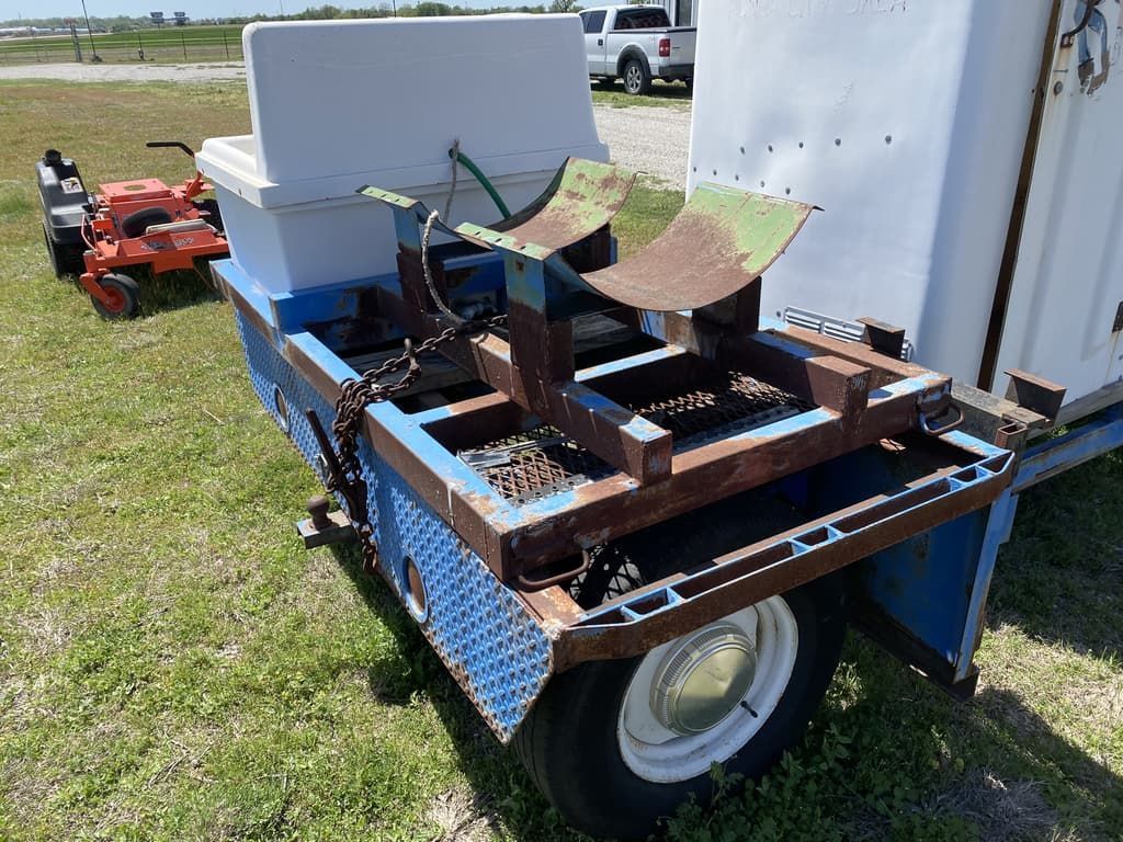 A trailer with a cooler and a lawn mower on it is parked in the grass.