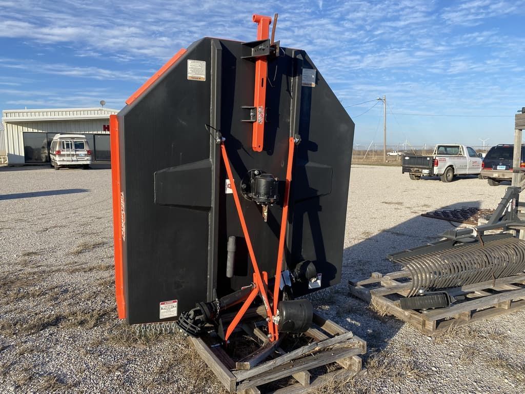 A black and orange machine is sitting on a wooden pallet in a gravel lot.