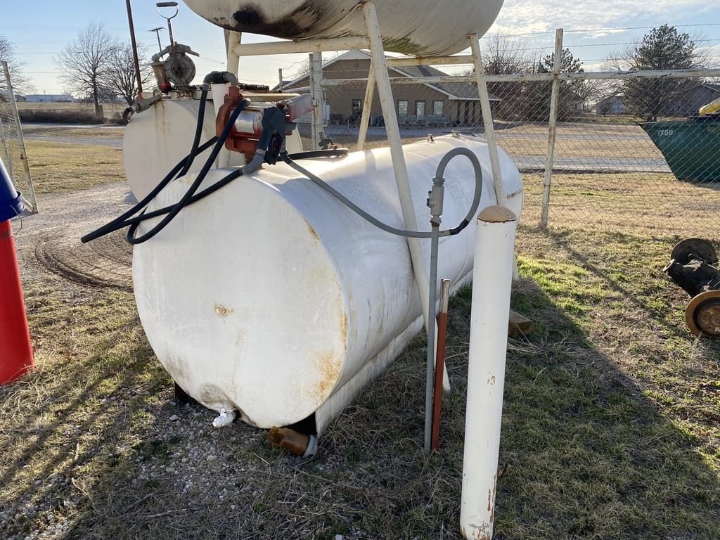 A large white tank is sitting in the grass next to a pole.