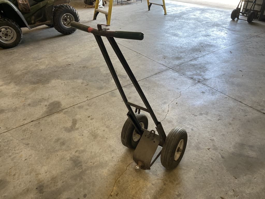 A cart with two wheels and a handle is sitting on the floor in a garage.