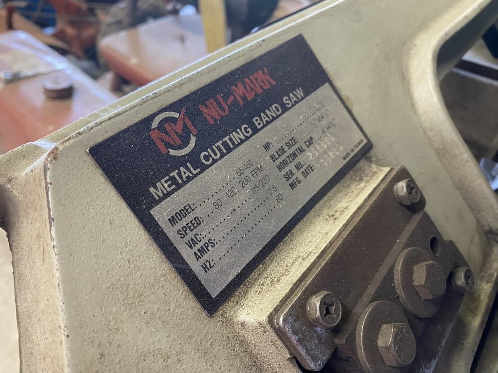 A close up of a metal cutting band saw with a label on it.
