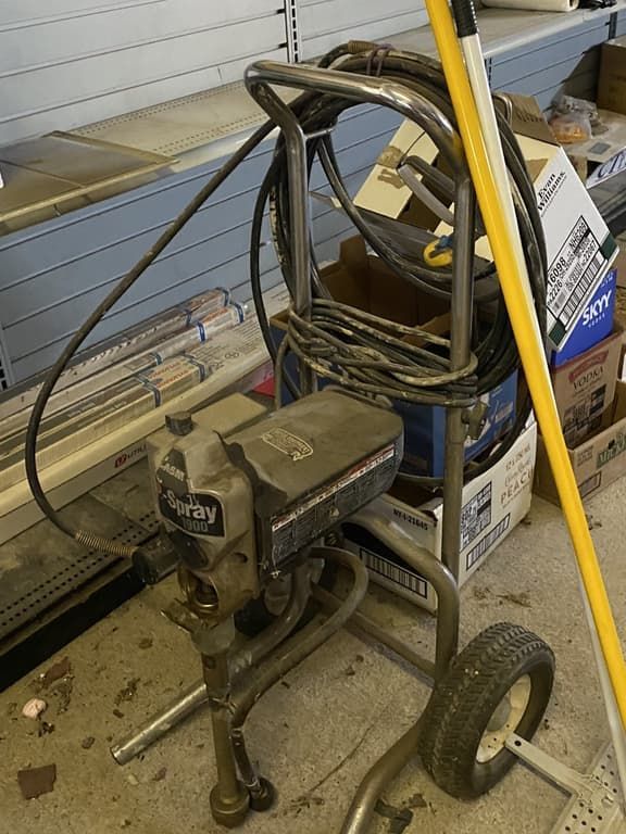 A spray paint machine is sitting on the floor next to a broom