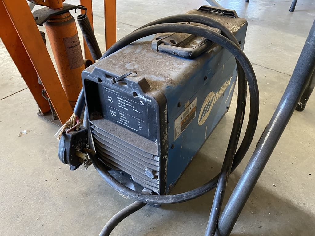 A welding machine is sitting on the floor next to a ladder.