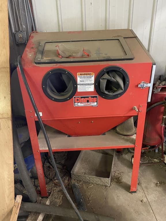 A red sandblasting machine is sitting on a shelf in a garage.