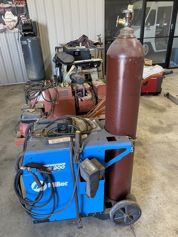 A welding machine is sitting in a garage next to a gas cylinder.