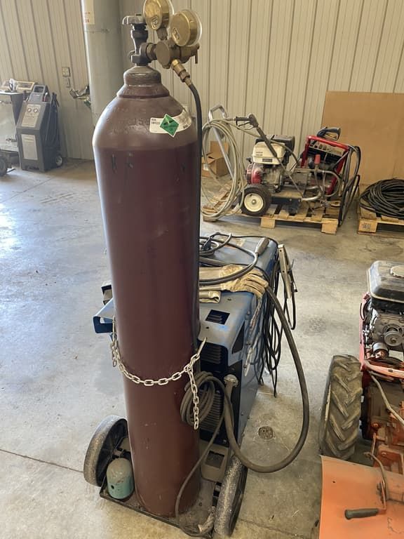 A gas cylinder is sitting on top of a welding machine in a garage.