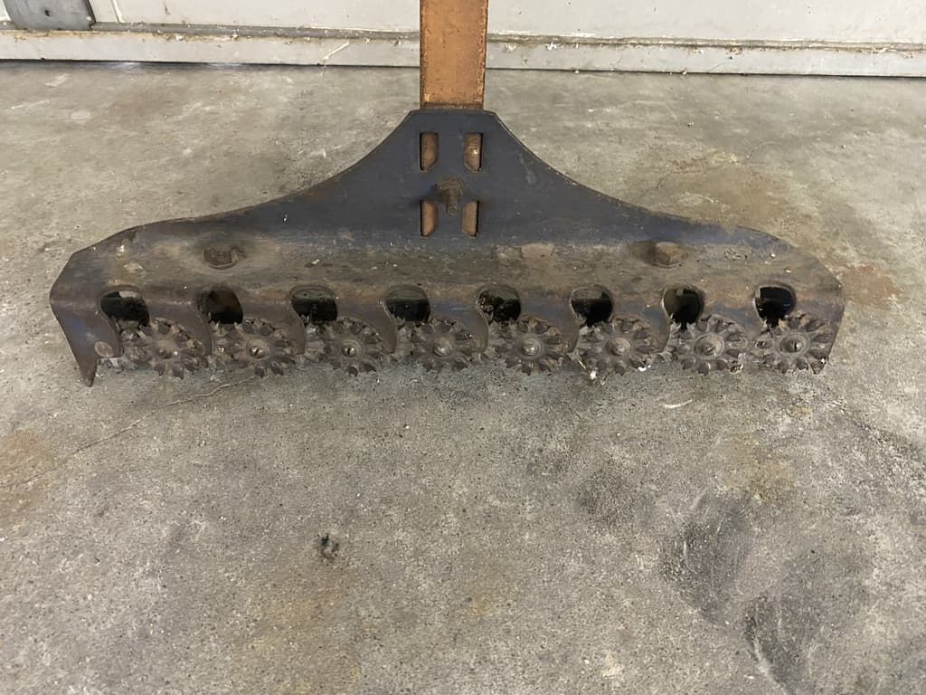 A metal rake with a wooden handle is sitting on a concrete floor.