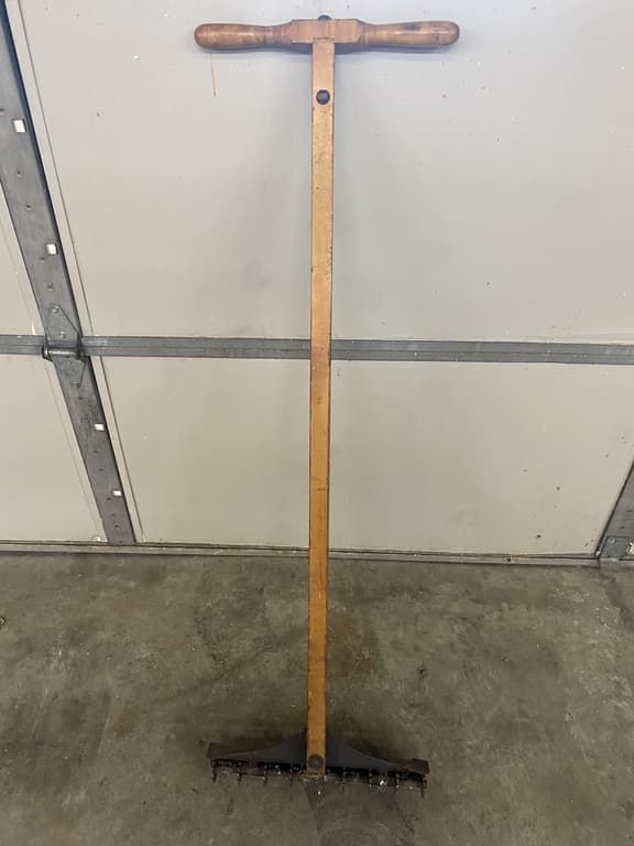 A rake with a wooden handle is sitting on the ground in front of a garage door.