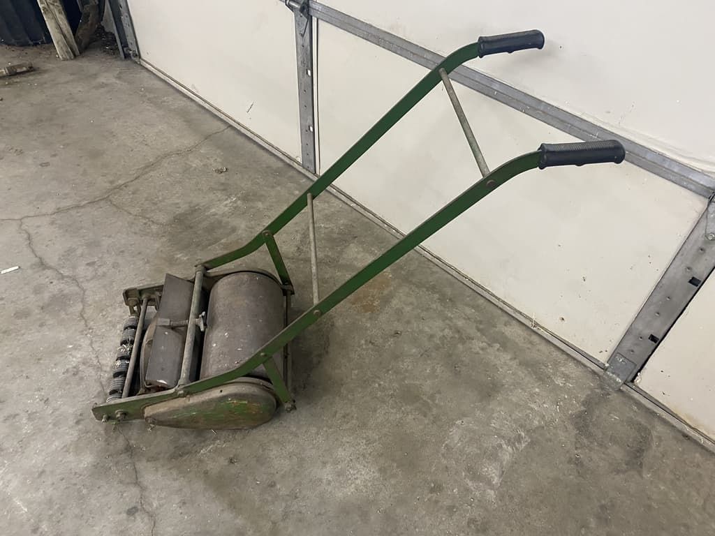 An old manual lawn mower is sitting on the floor in a garage.