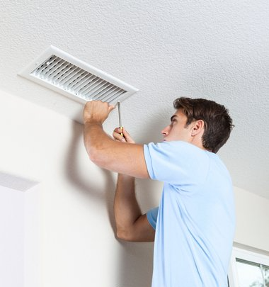Picture of a man in a blue polo unscrewing an air duct vent.