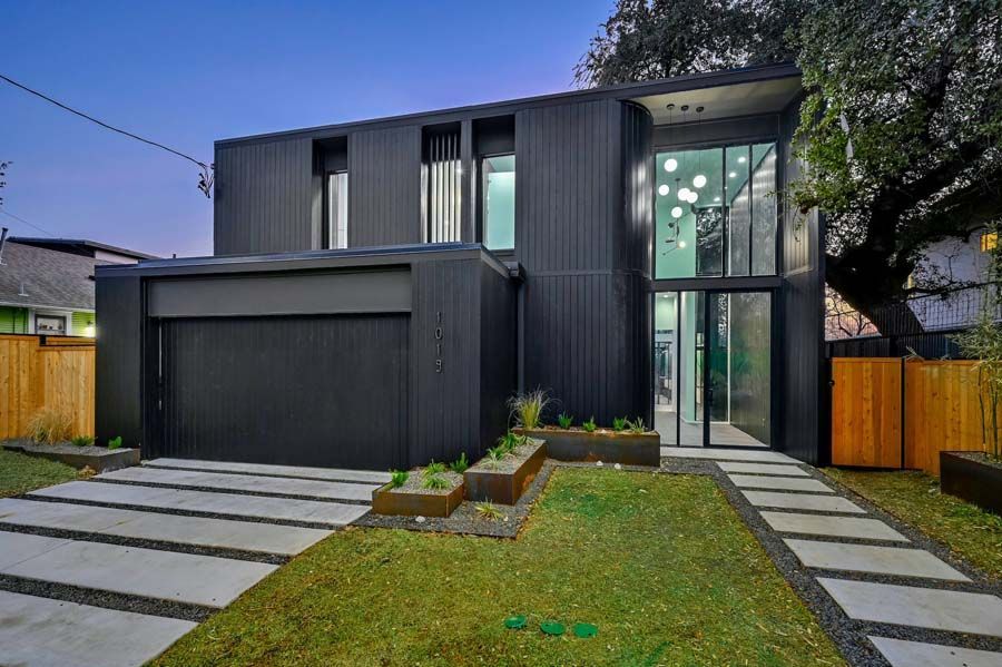 A modern black house with a large driveway and a large garage.
