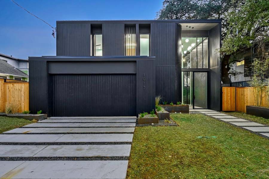 A black house with a concrete driveway leading to it.