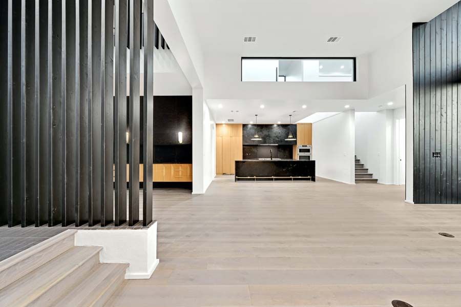 A large empty room with hardwood floors and stairs leading to a kitchen.
