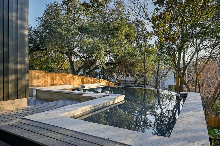 A large swimming pool is surrounded by trees and a wooden deck.