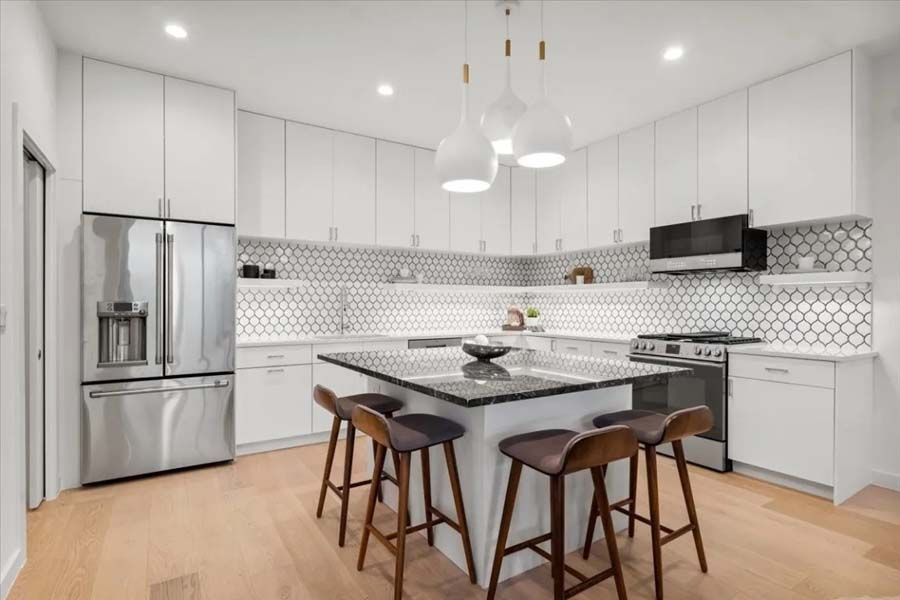 A kitchen with white cabinets , stainless steel appliances , and a large island.