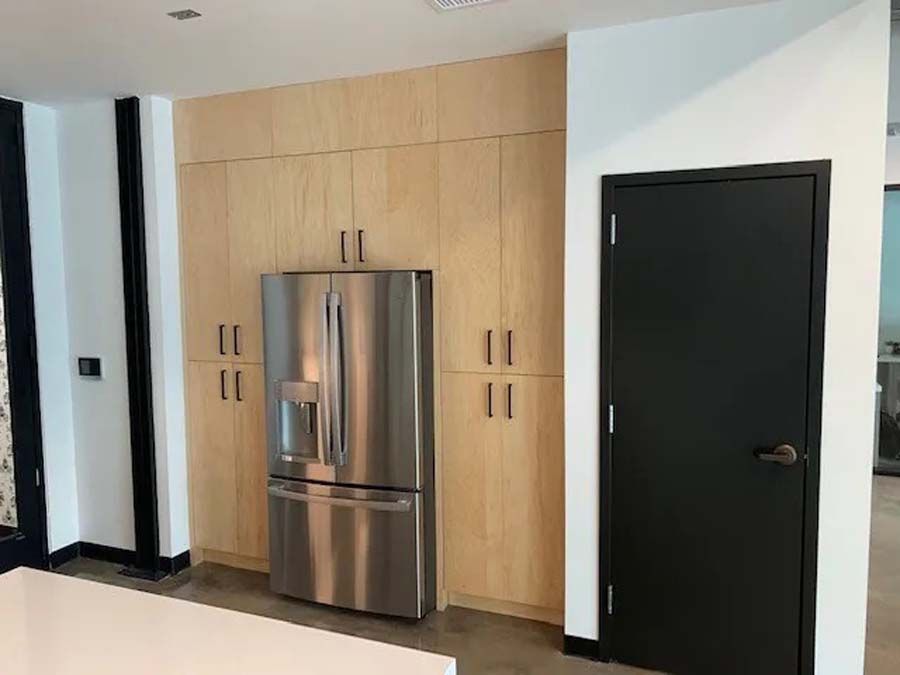 A stainless steel refrigerator is sitting in a kitchen next to a black door.