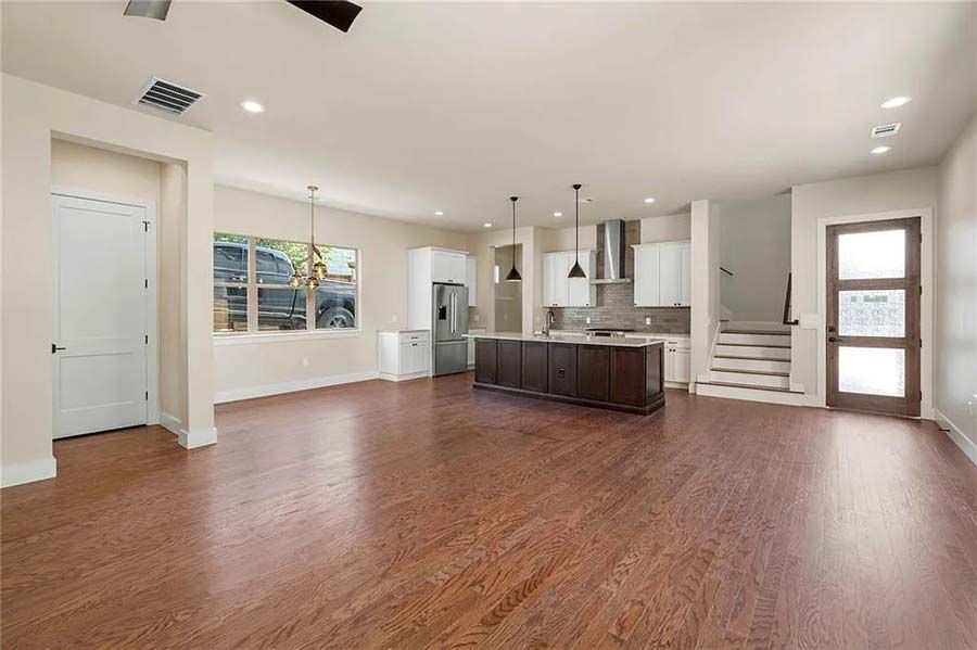 A living room with hardwood floors and a kitchen in the background.