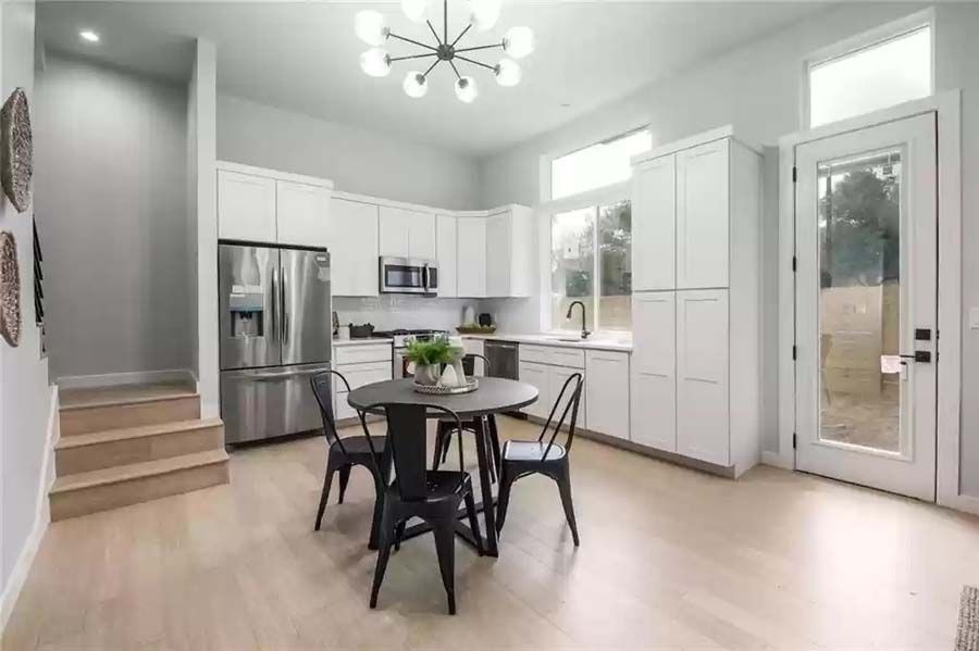 A kitchen with white cabinets , stainless steel appliances , a table and chairs.