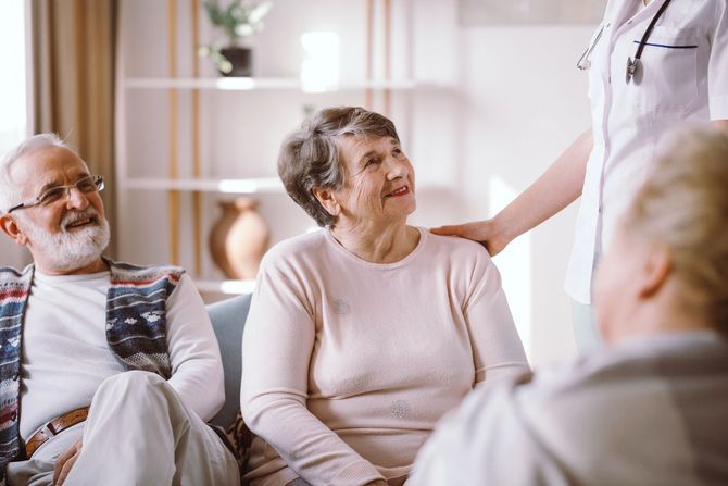In un salotto, un operatore sanitario con lo stetoscopio al collo posa una mano rassicurante sulla spalla di una persona.