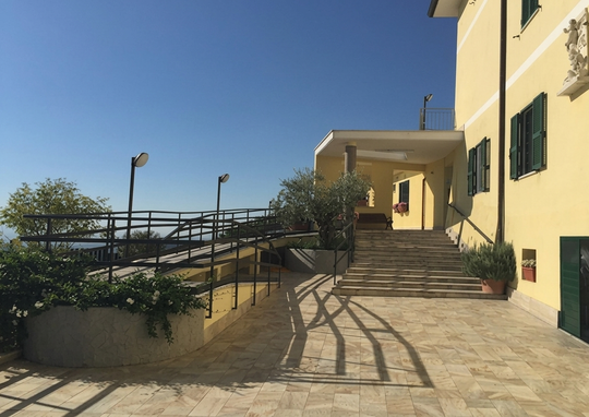 Una passerella esterna con scale e rampa che conduce a un edificio giallo sotto un cielo azzurro e limpido.