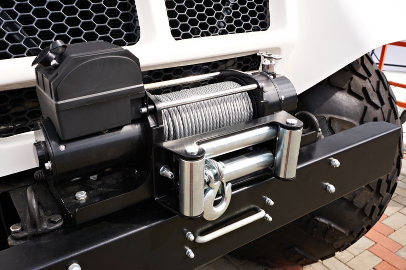 Black winch mounted on a white vehicle's bumper with a metal cable and hook.