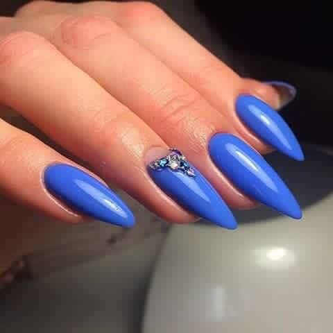 Un primo piano della mano di una donna con lunghe unghie blu e strass.