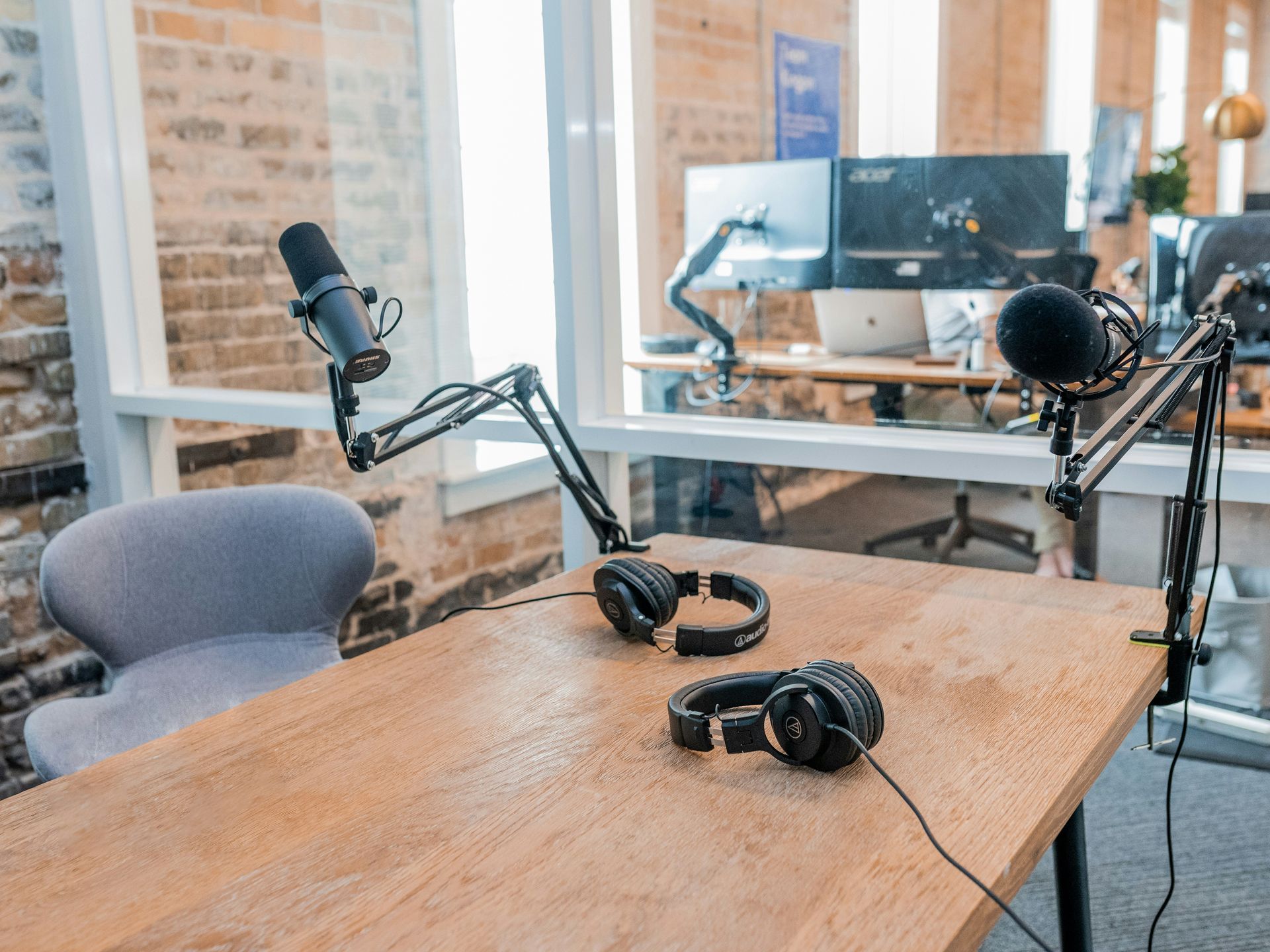 A microphone and headphones are on a wooden table in an office used as a podcast studio.