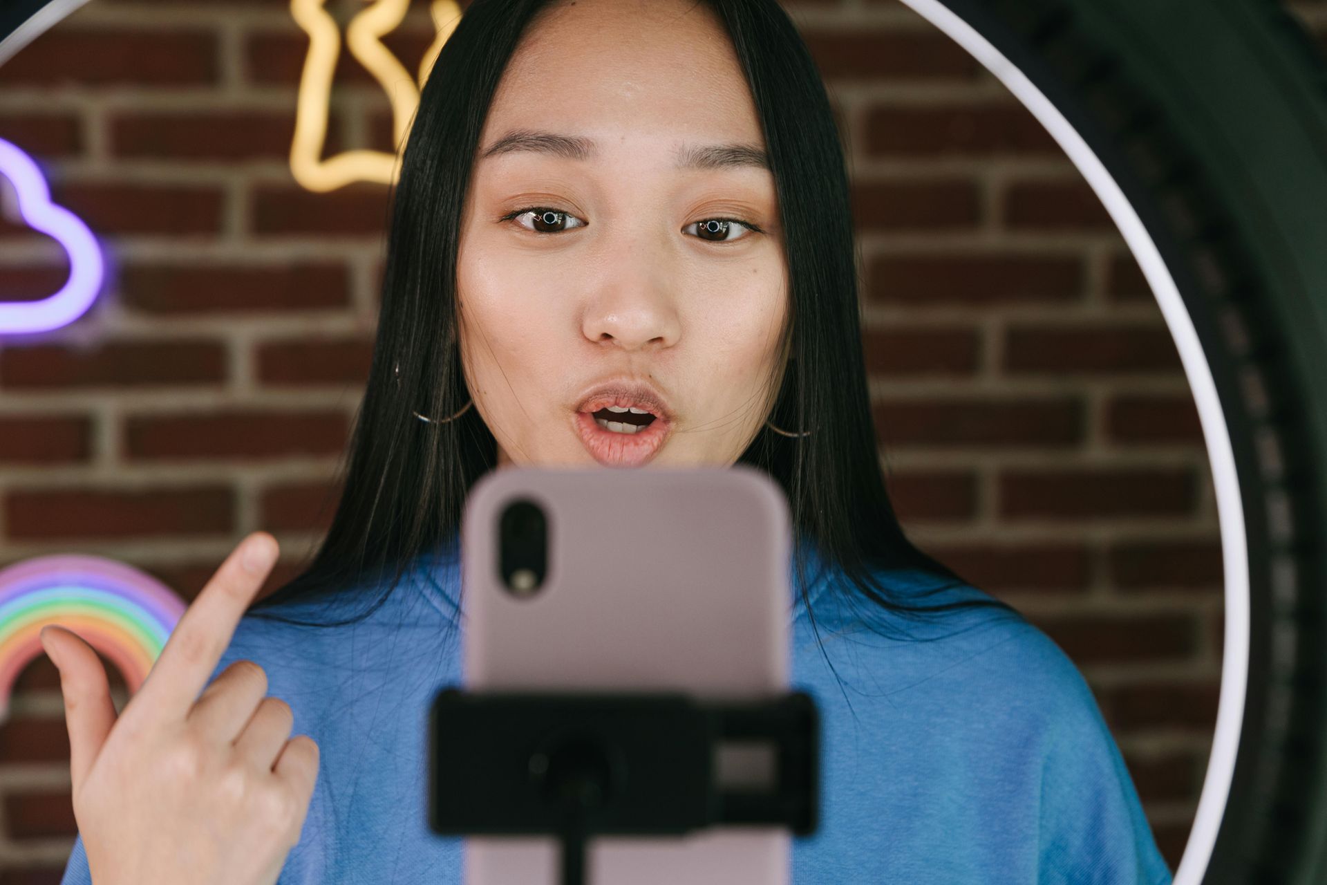 A woman is recording herself with her cell phone in front of a ring light.