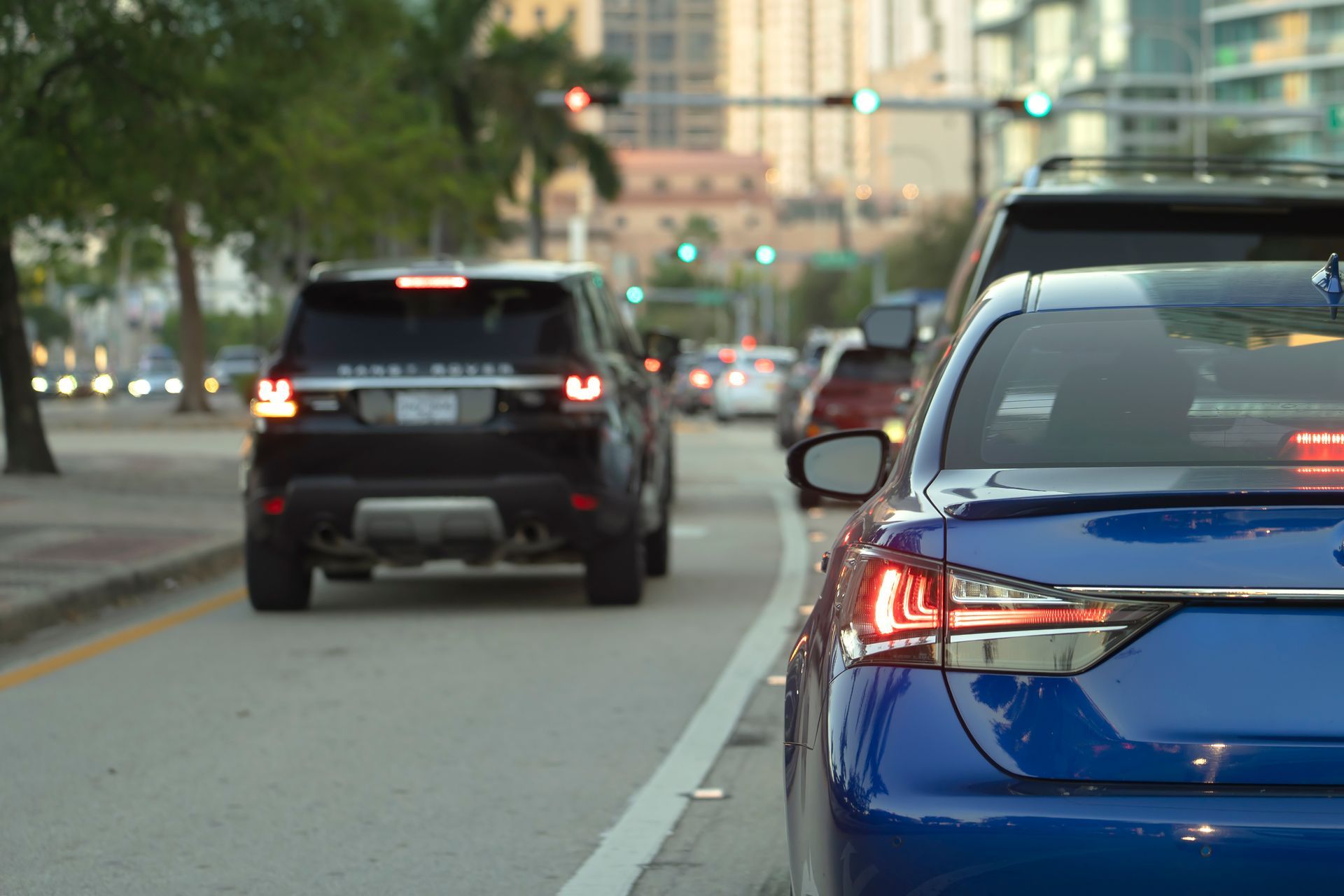 A blue car is driving down a city street next to a black suv.